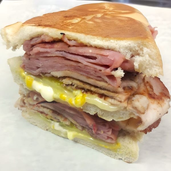 A toasted Selfie Subs sandwich, cut in half, revealing layers of meat, mustard, and mayonnaise.