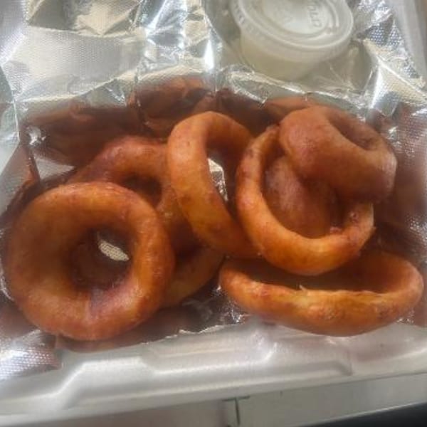 Golden-brown onion rings and a small cup of dipping sauce in a foil-lined takeout container.