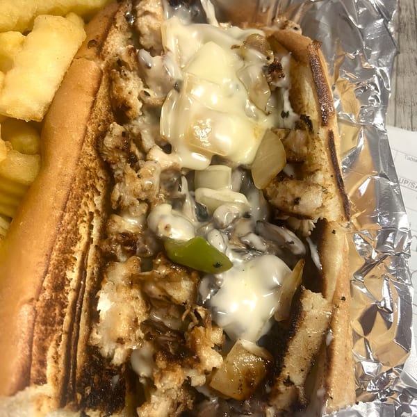 A Selfie Subs cheesesteak with melted cheese, onions, and green peppers, served with fries.