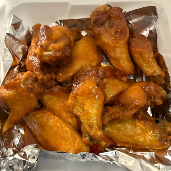 Close-up of a dozen saucy chicken wings in a white styrofoam container lined with aluminum foil.